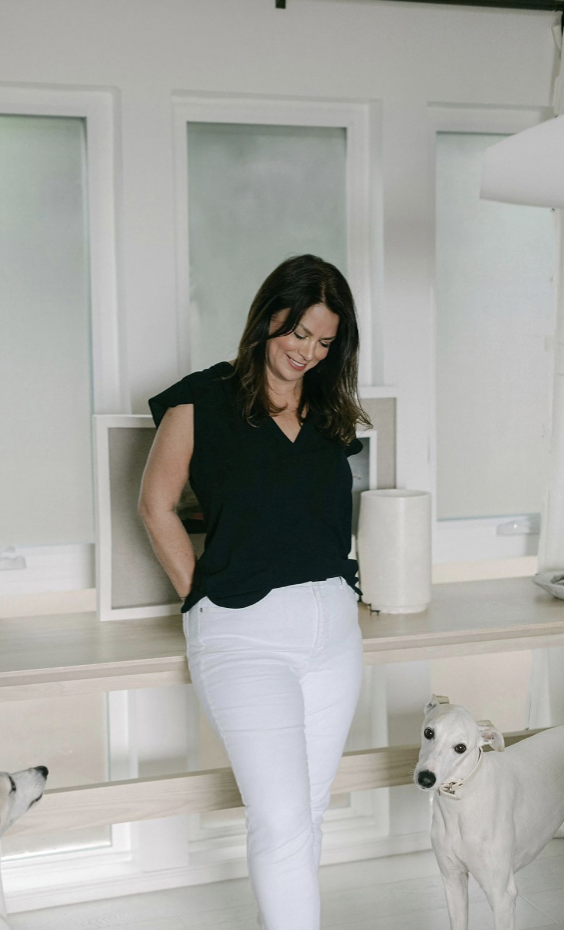 a photo of claudia standing against a counter looking down at her white dog.